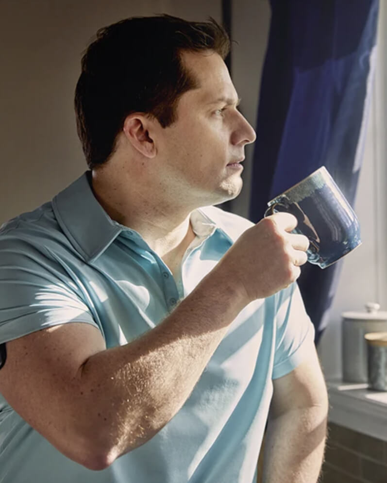 An Eversense CGM user holding a blue mug using the Eversense transmitter on his arm